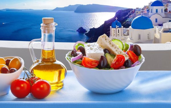 Greek Salad against the backdrop of a famous church in Oia village, Santorini island in Greece