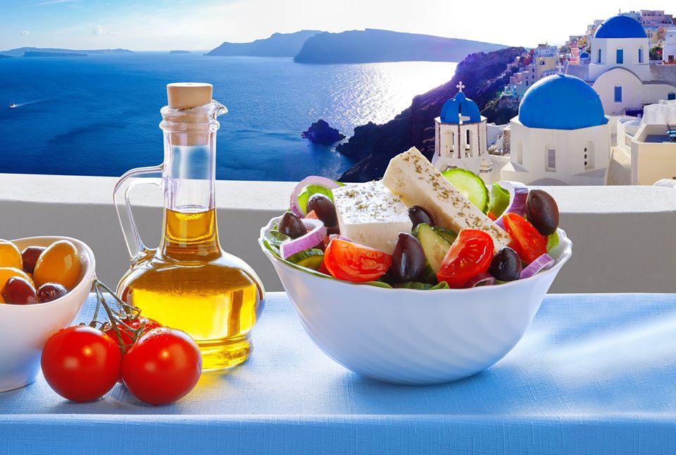 Greek Salad against the backdrop of a famous church in Oia village, Santorini island in Greece