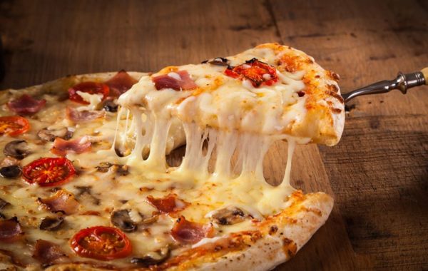 Hot pizza slice with melting cheese on a rustic wooden table.