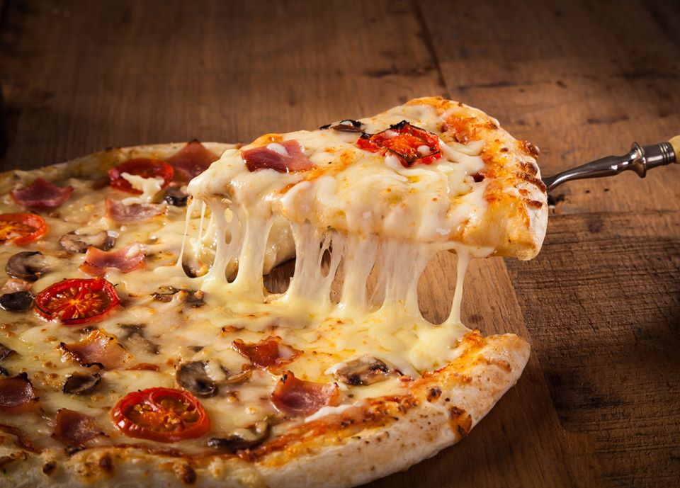 Hot pizza slice with melting cheese on a rustic wooden table.