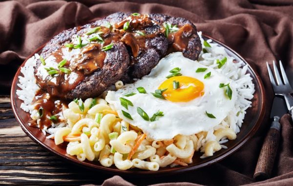 Loco Moco, Hawaiian Gravy Burger on Rice, and macaroni salad topped with a fried egg on an earthenware plate on a rustic wooden table with brown cloth