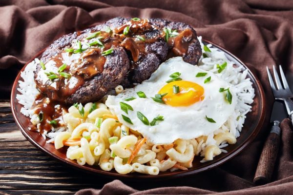 Loco Moco, Hawaiian Gravy Burger on Rice, and macaroni salad topped with a fried egg on an earthenware plate on a rustic wooden table with brown cloth
