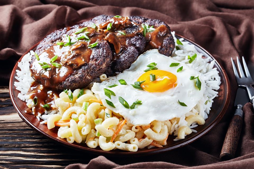 Loco Moco, Hawaiian Gravy Burger on Rice, and macaroni salad topped with a fried egg on an earthenware plate on a rustic wooden table with brown cloth
