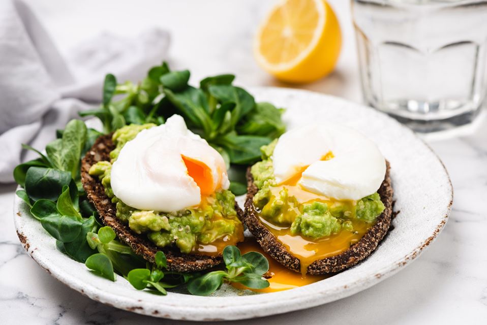 Guacamole rye bread toast with poached egg on plate.