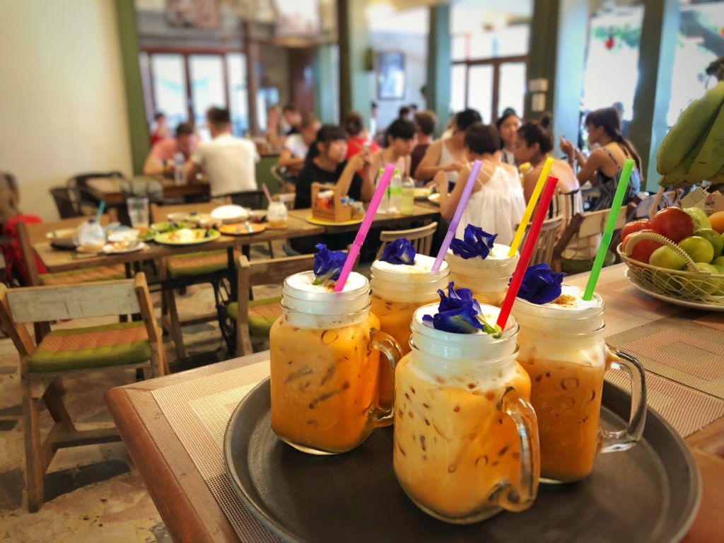 “Thai milk tea” or “cha nom yen” with flowers and wooden tray background at coffee shop in thailand.